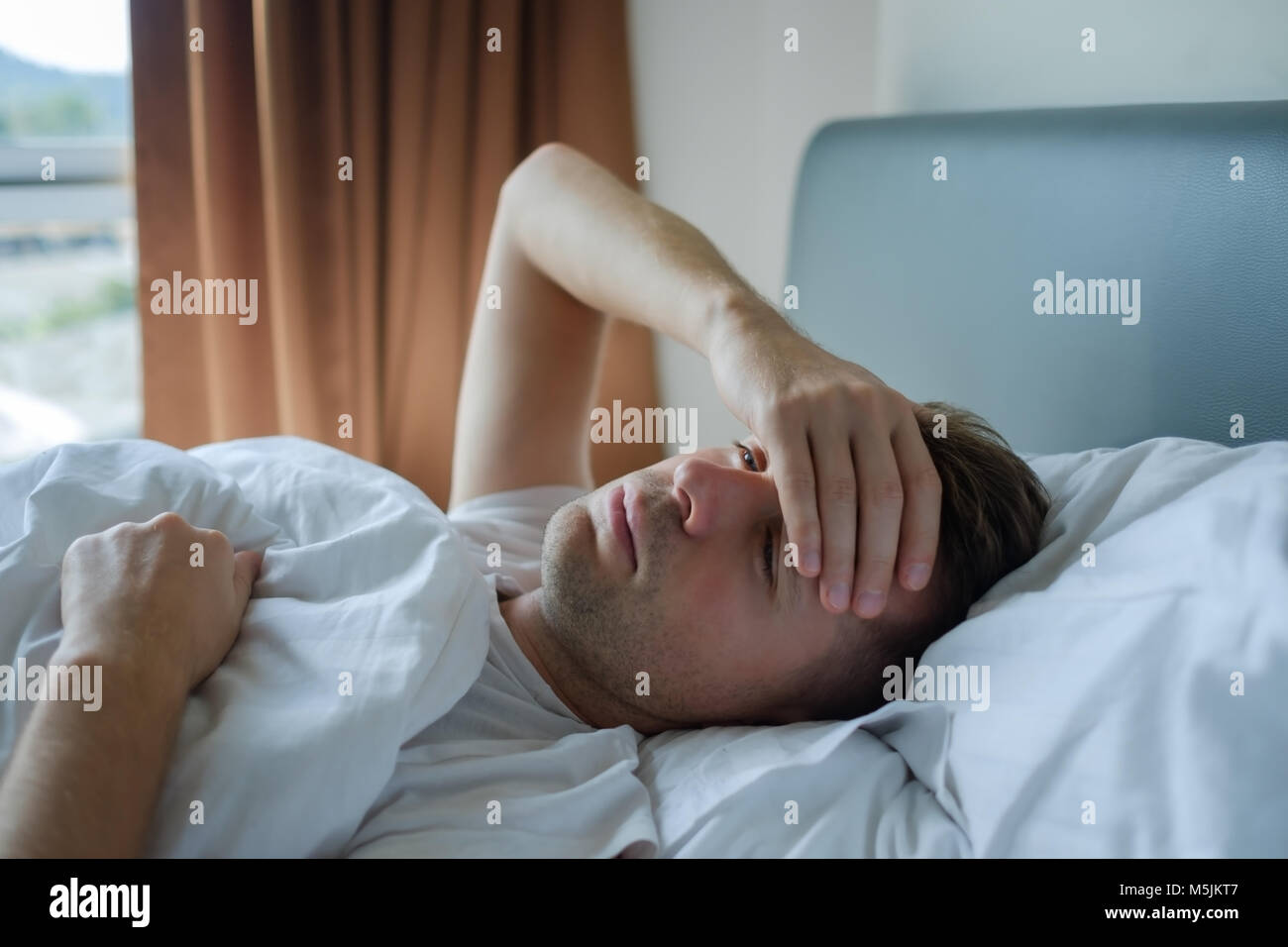 Hombre tumbado en la cama en casa sufre de dolores de cabeza o resaca Foto de stock