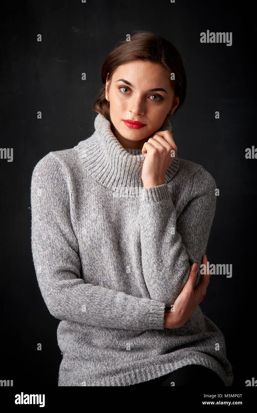 Retrato de hermosa mujer sonriente vistiendo un suéter cuello tortuga  mientras posan contra un fondo oscuro Fotografía de stock - Alamy