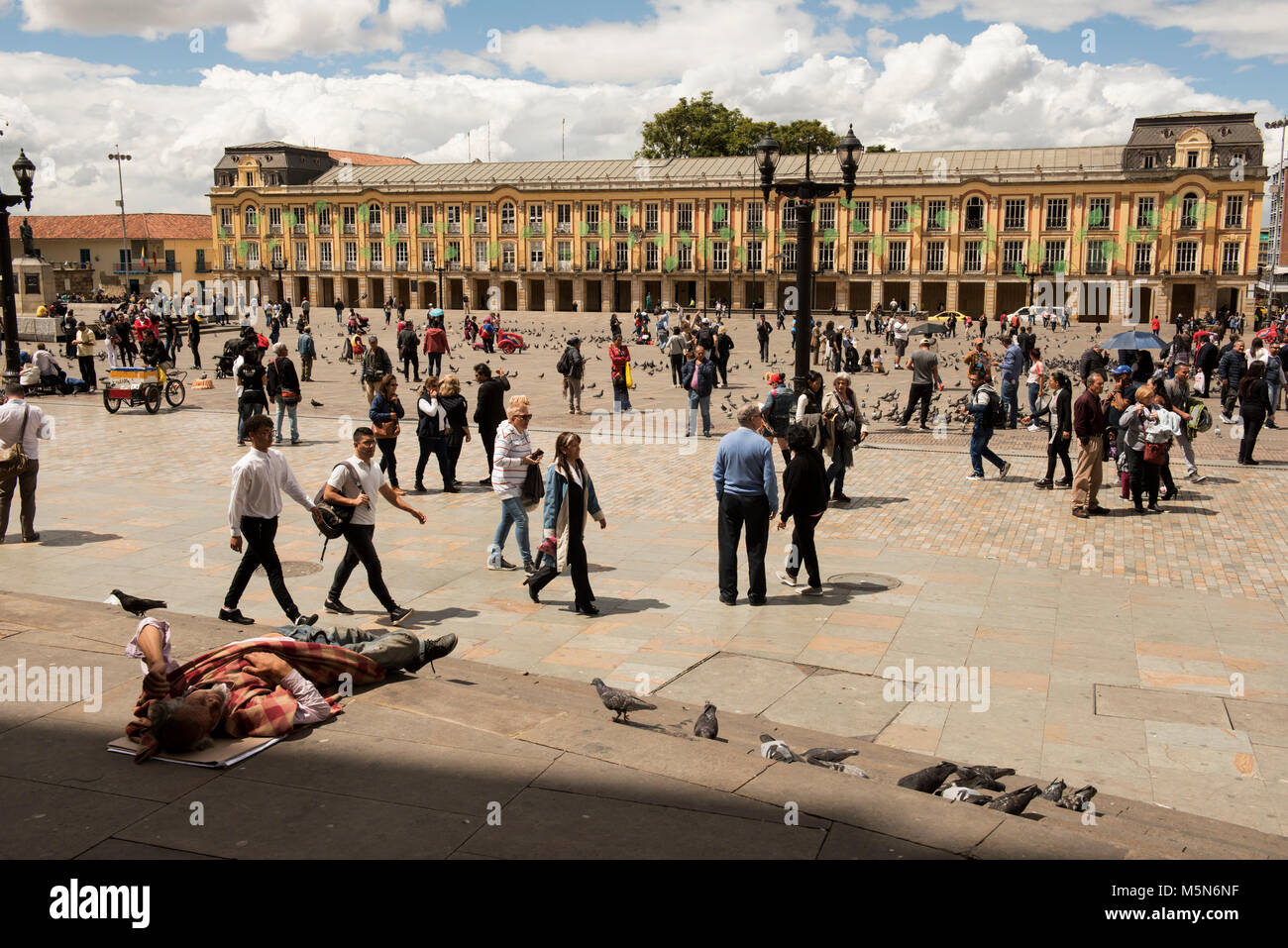 La Plaza de Simón Bolívar en Bogotá, Colombia, con los edificios del gobierno y las personas que caminan y vagabundo tumbado en pasos en primer plano Foto de stock