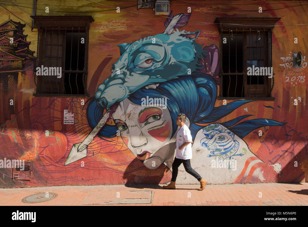 Un hombre caminando por una pared con graffiti en la Candelaria, en Bogotá, Colombia. Graffiti ha sido transformados en armas en la ciudad capital de Colombia. Foto de stock