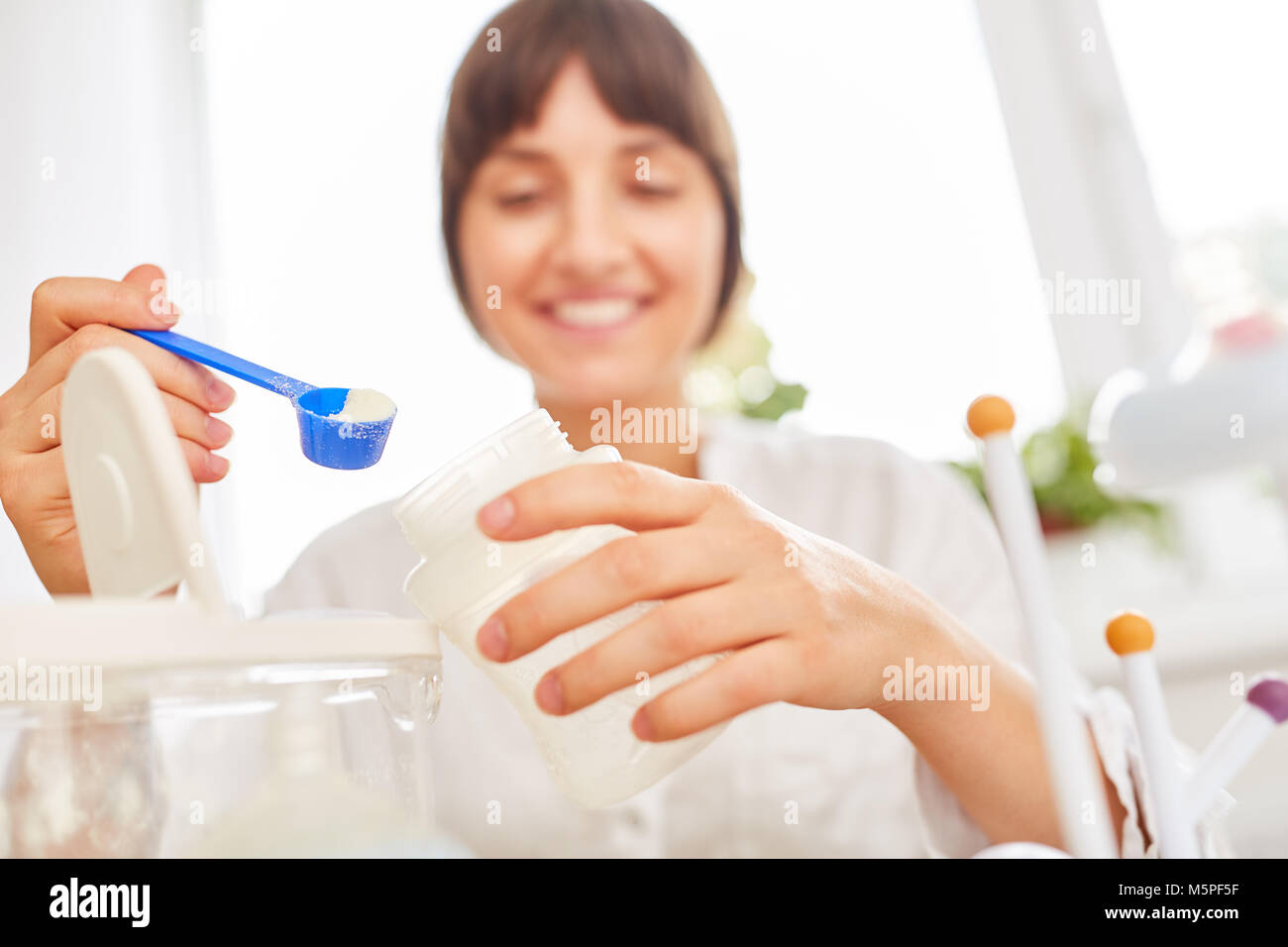 Mujer joven como madre da los probióticos con la cuchara de medición en los alimentos para bebés Foto de stock