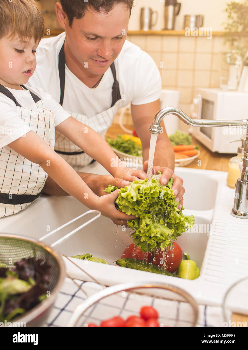 El hombre y el muchacho lavando verduras antes de comerlas. Foto de stock
