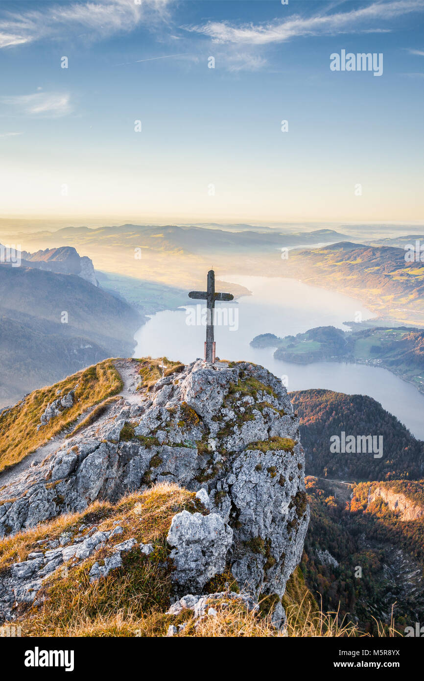 Vista panorámica de un idílico paisaje de montaña en los Alpes con una cruz de madera en la cima de una montaña en golden luz del atardecer al atardecer. Foto de stock