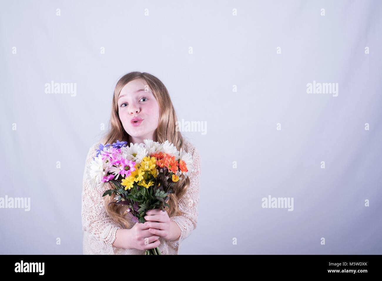 12-year-old girl con largo pelo rubio sucio celebración colorido bouquet de margaritas con mirada de admiración contra el fondo blanco. Foto de stock