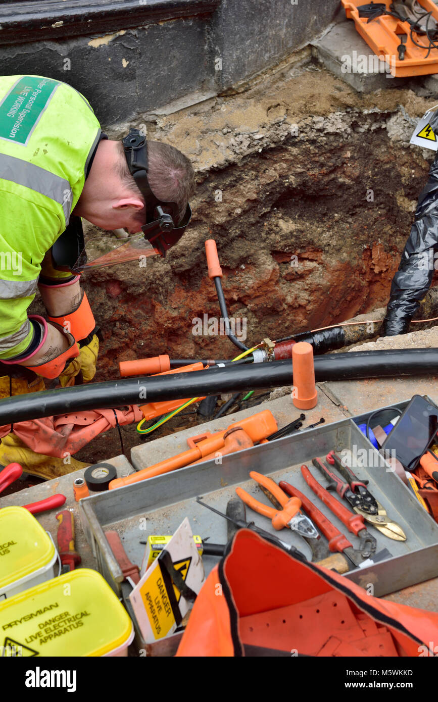 Obrero de electricidad la reparación de las tuberías enterradas de cable eléctrico en el agujero en el pavimento de trabajo Foto de stock