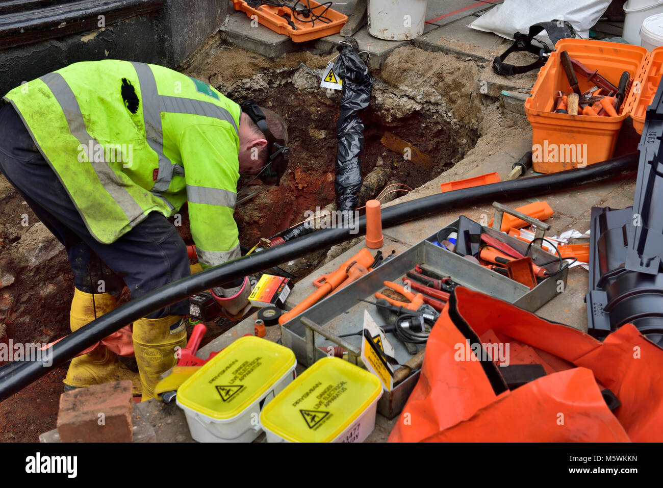 Obrero de electricidad la reparación de las tuberías enterradas de cable eléctrico en el agujero en el pavimento de trabajo Foto de stock