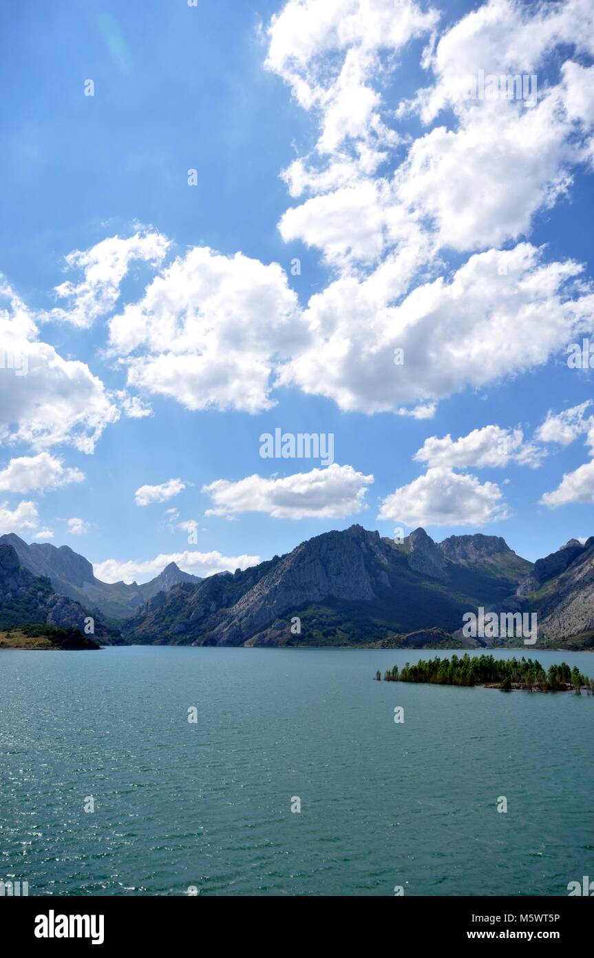 Vistas a un lago en el norte de España. Isla en el lago y la cordillera detrás con cielo azul y nubes. Foto de stock