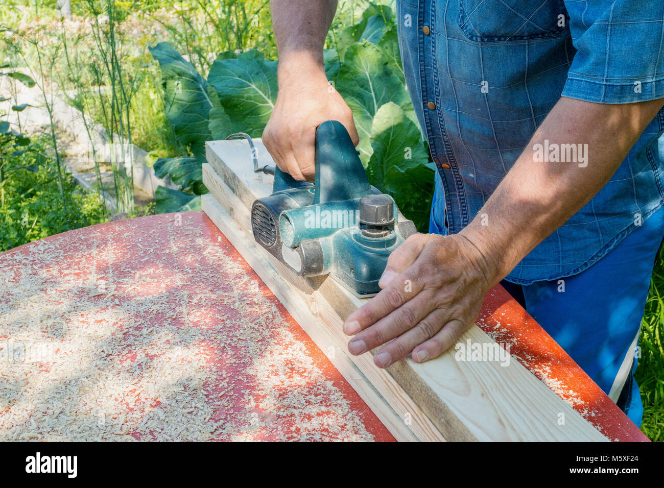 El maestro agudiza el panel de madera con una lijadora eléctrica en un día  soleado en el jardín. El peligro. Infracción de las normas de seguridad  Fotografía de stock - Alamy