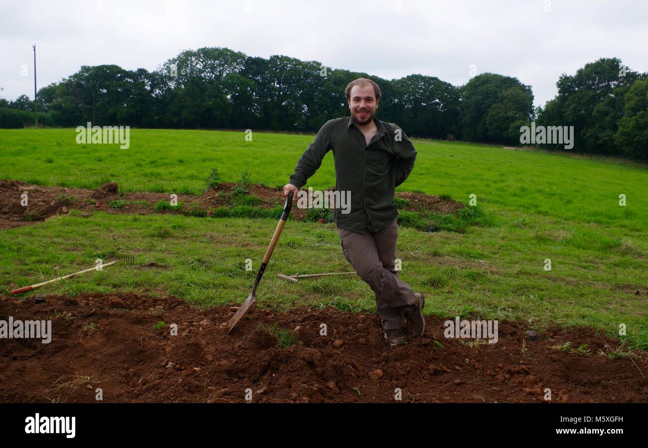 Joven apuesto hombre cavando manualmente un campo de hierba a mediados de Devon para construir un túnel de Poly. Viveros, Lydcott Morchard Bishop, Crediton, Reino Unido. Agricultura. Foto de stock