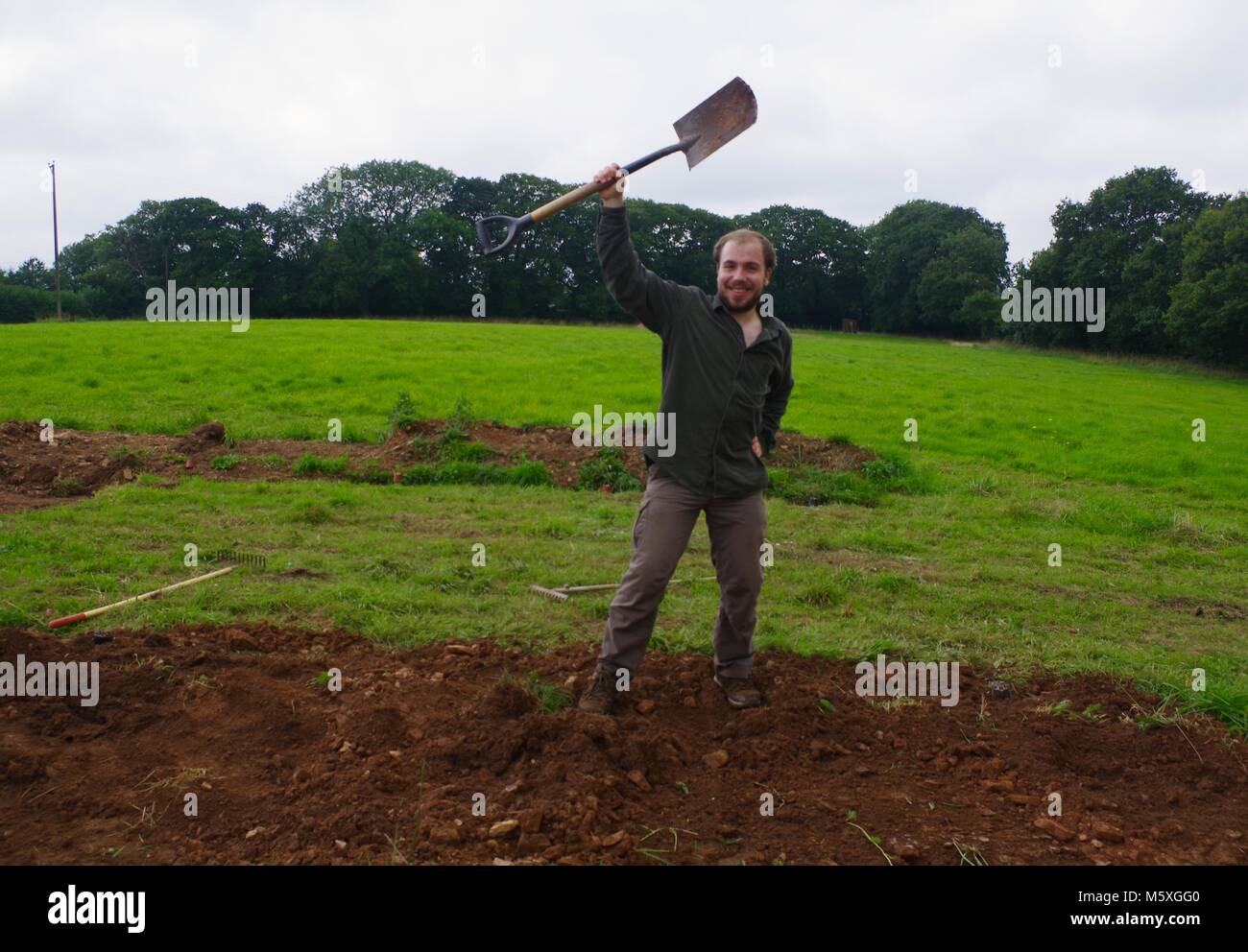 Joven apuesto hombre cavando manualmente un campo de hierba a mediados de Devon para construir un túnel de Poly. Viveros, Lydcott Morchard Bishop, Crediton, Reino Unido. Agricultura. Foto de stock