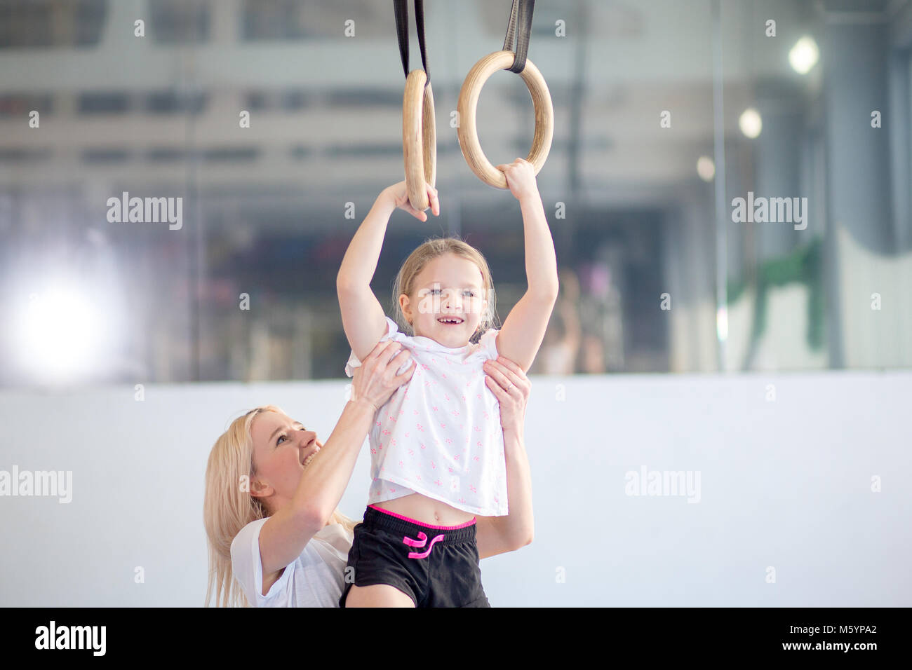 Madre ayudando a hija a jugar deportes en anillos de gimnasia Foto de stock