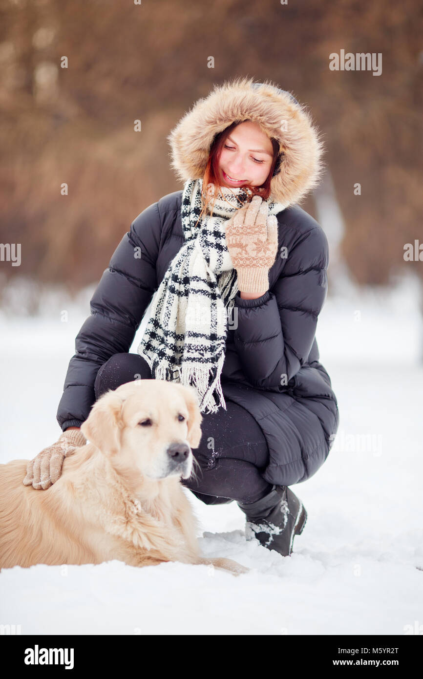 Foto de mujer alegre y en cuclillas junto al labrador en invierno Foto de stock