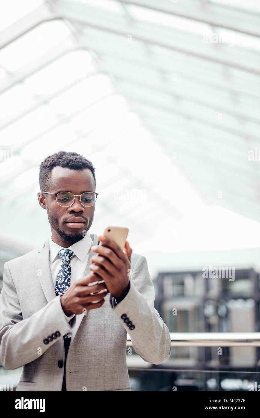 Los mensajes de texto por teléfono afroamericanas empresario en mall o salón de la oficina moderna Foto de stock
