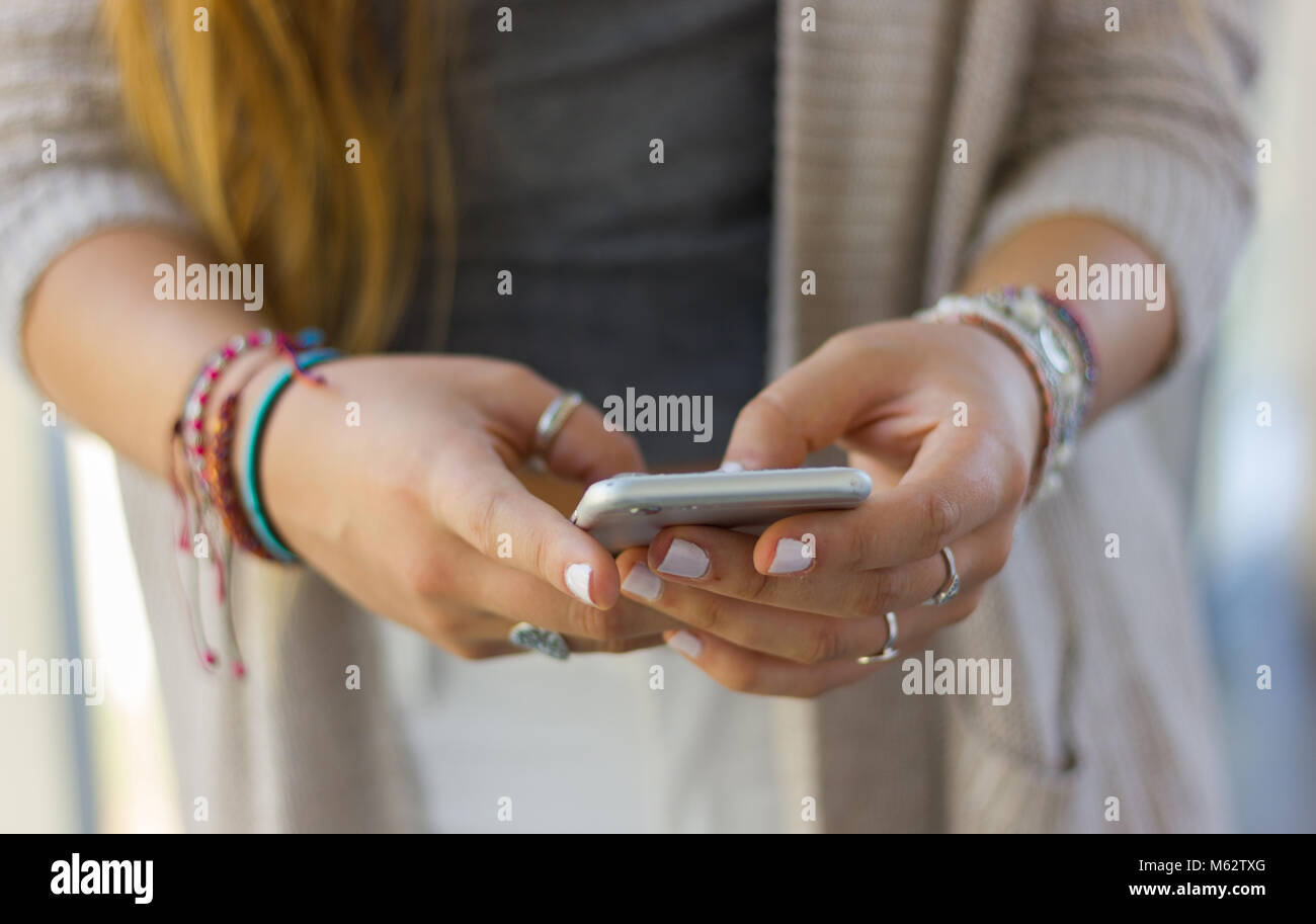Teléfono celular en manos de adolescentes chica rubia con cone uñas pintadas, pulseras y anillos. Generación Millennial, medios sociales, smartphone adicción Foto de stock