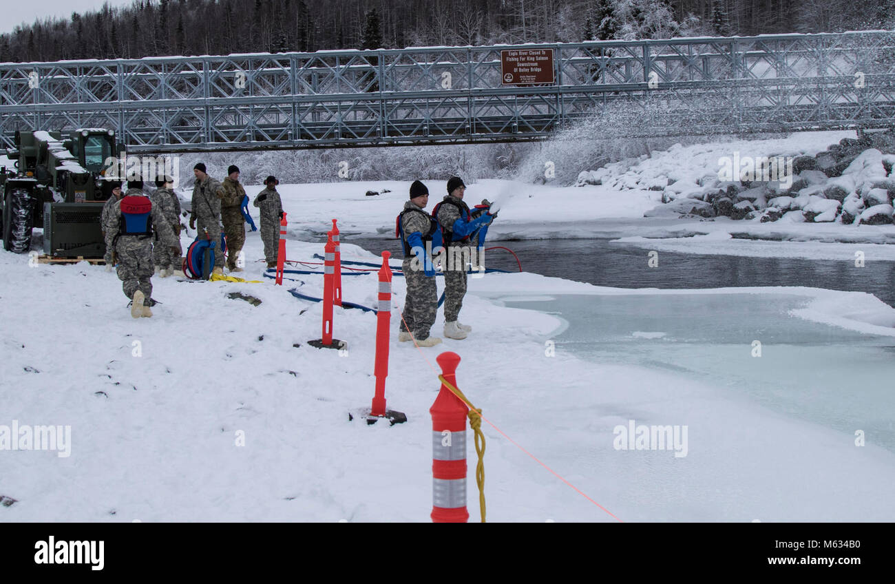 Soldados de la Guardia Nacional de Alaska con la utilidad Ingeniero 207desapego y el equipo de gestión de la construcción 208pulverizar agua sobre la tierra y el río para espesar y alargar la masa de hielo, como parte de una operación de puente de hielo en la base conjunta Elmendorf-Richardson, Febrero 10, 2018. Puente de hielo es un método que permite a los vehículos militares para viajar sobre hielo que está a una profundidad bastante segura para conducir, sin romper. (Ee.Uu. Guardia Nacional del Ejército Foto de stock