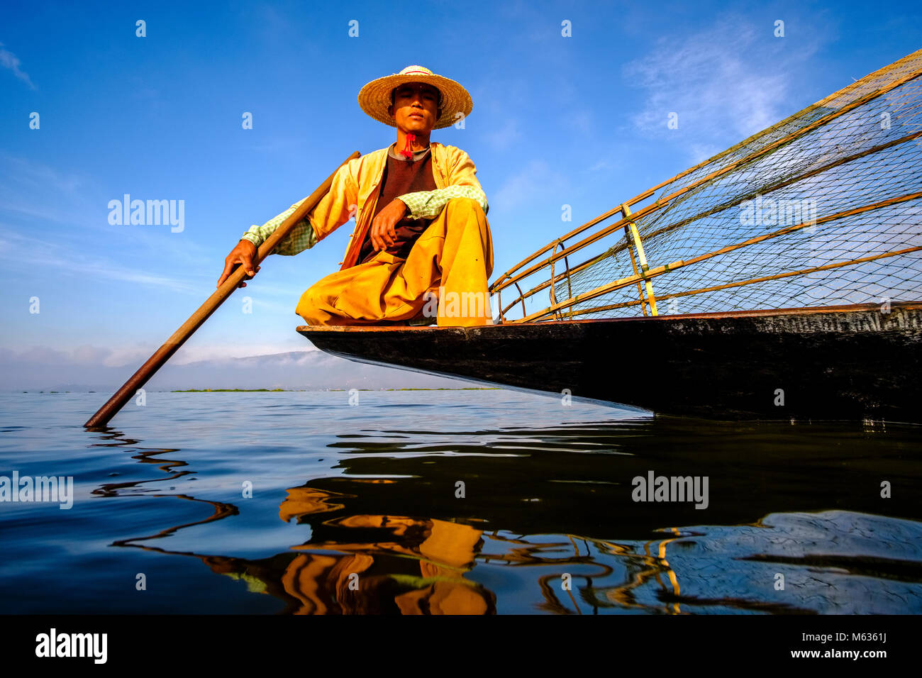 Un pescador, sentado en su barco paddeling, es la forma tradicional de pesca en el Lago Inle Foto de stock