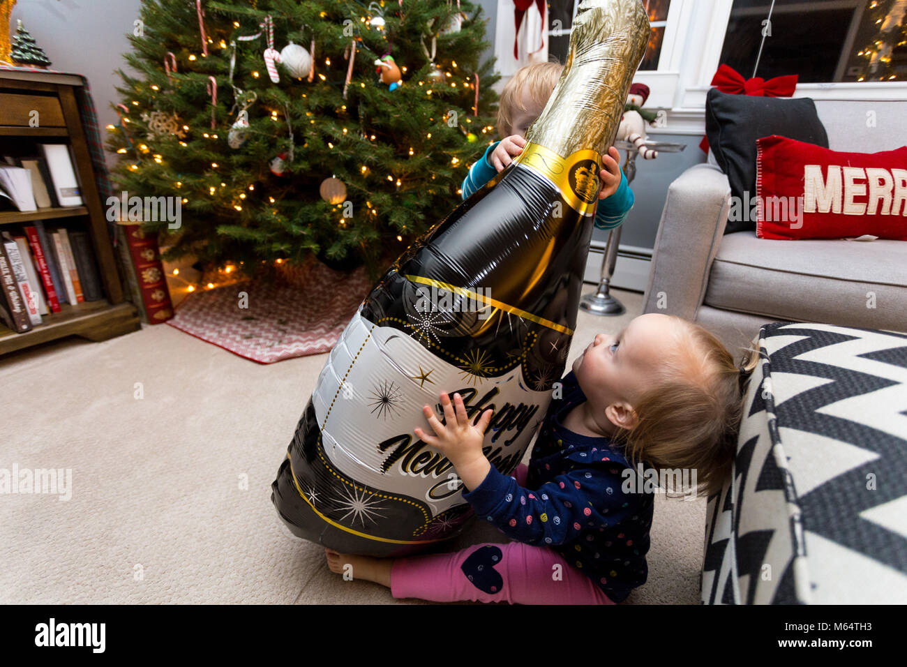 Una niña y un niño caucásico juega con un globo de Nochevieja en una casa suburbana Salón Foto de stock