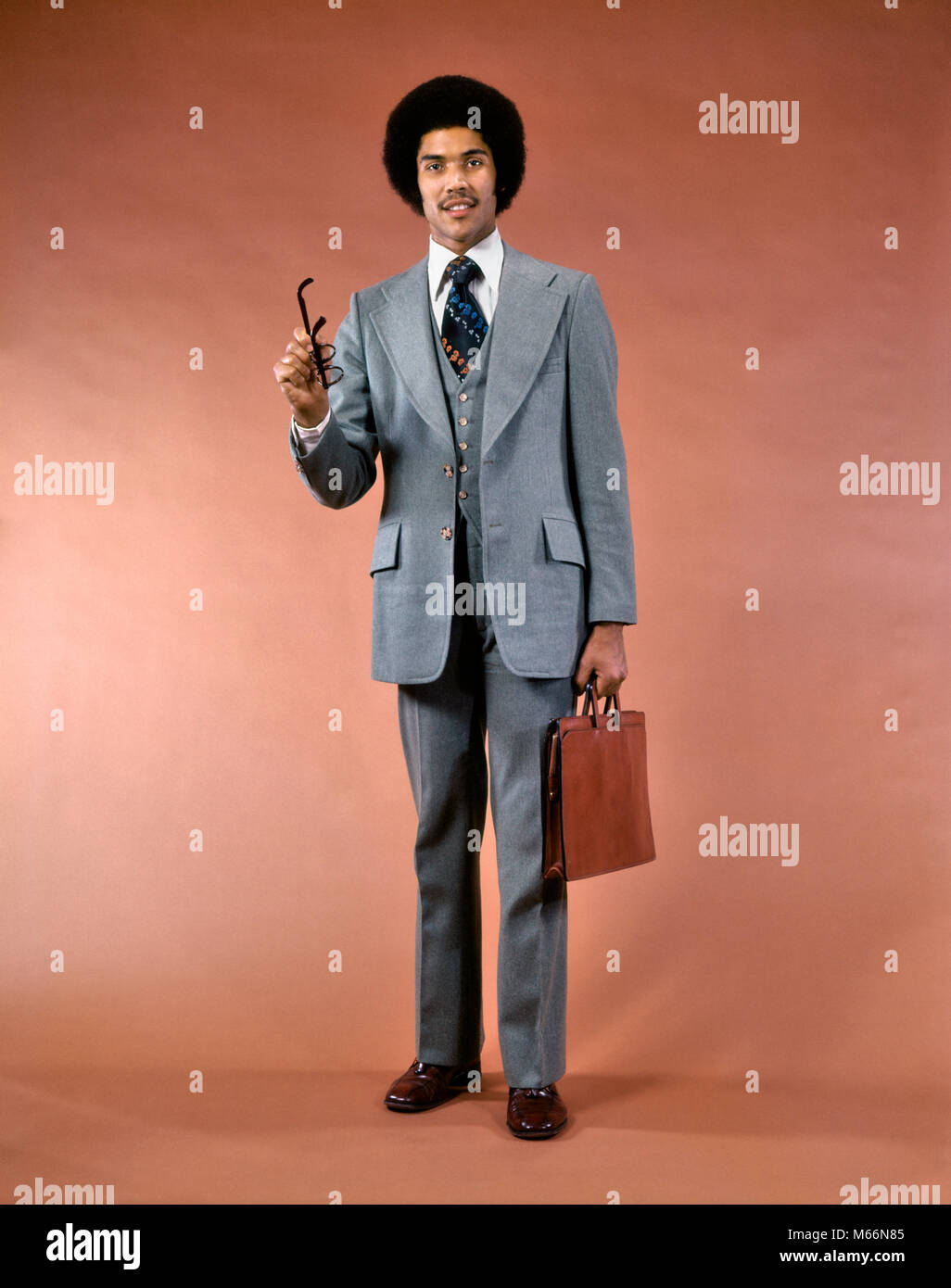 1970 sonriente hombre afroamericano TRAJE DE TRES PIEZAS MALETÍN mirando a  la cámara apuntando gesticulando con anteojos - ks12055 HAR001 HARS  elegante collar de color antiguo ejecutivo de la industria de la