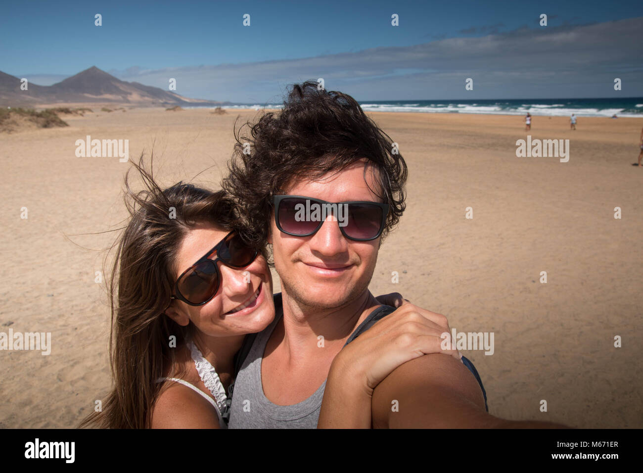 Feliz abrazando pareja joven retrato en la playa. Medio cercano con fondo escénico. Fuerteventura, Islas Canarias, España. Foto de stock