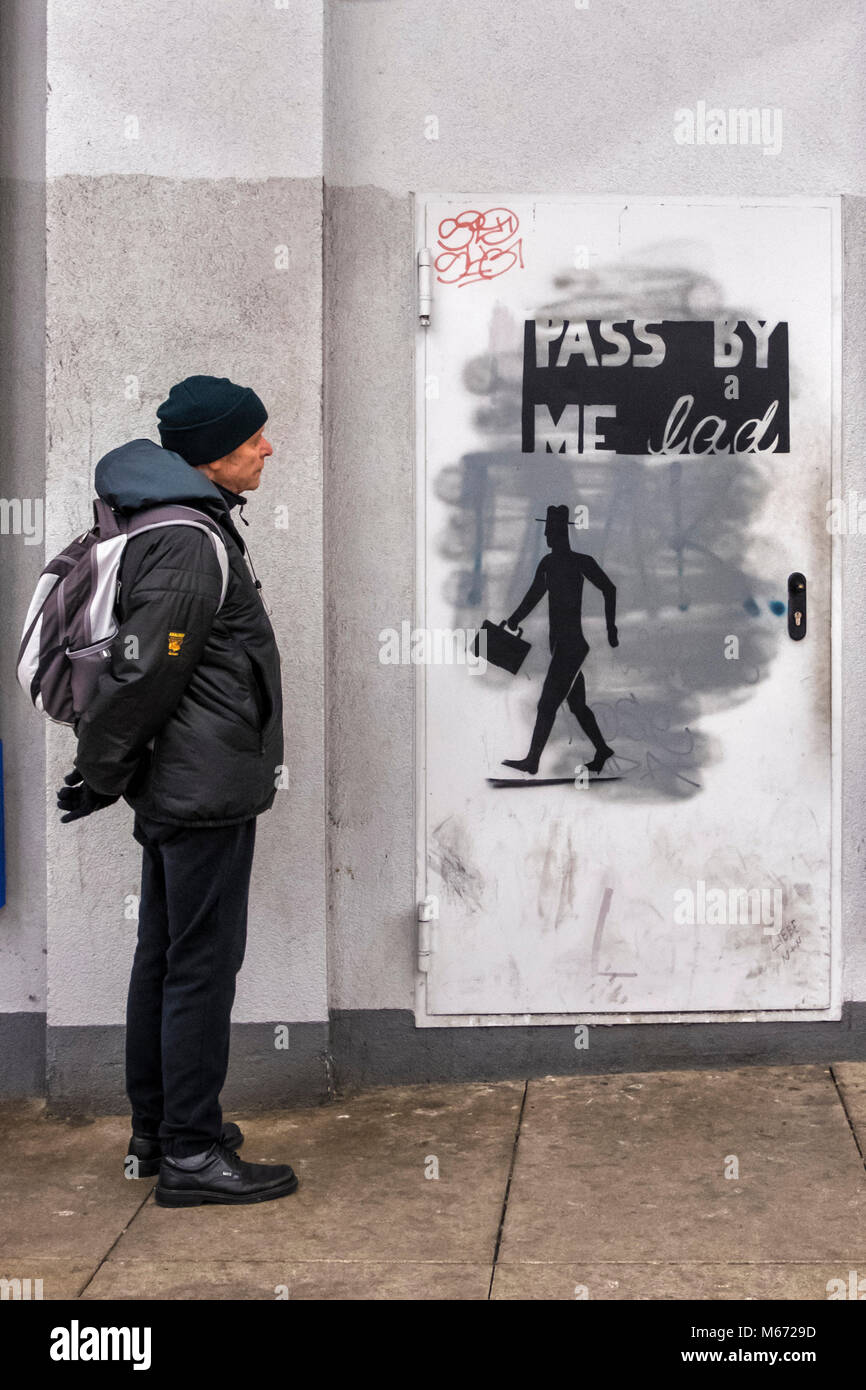 Berlín, Mitte, Alexanderplatz. Altos anciano con mochila mira el arte en la calle - Silueta de hombre con maletín y pasarme por Lad inscripción Foto de stock