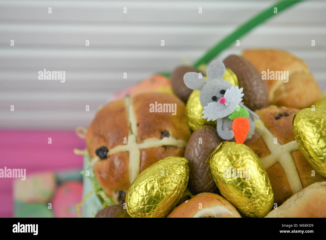 Comida de Pascua en una cesta con Hot Cross Buns y dorada de huevos de Pascua de chocolate con decoración de conejito de Pascua Foto de stock