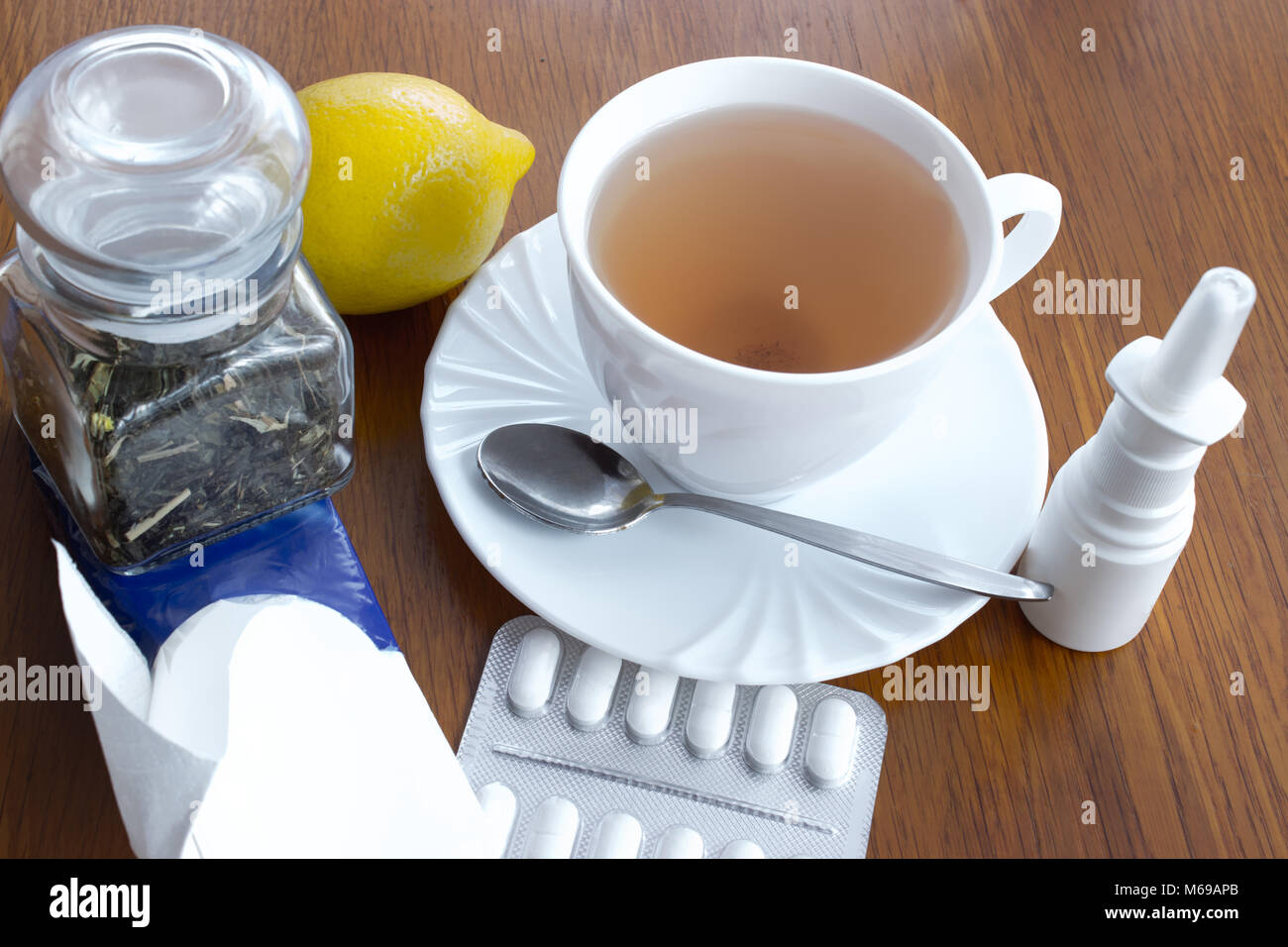 Una taza de té con platillo y cuchara, limón, medicamentos, una dosis de cristal con té, pañuelos de papel, gotas nasales. Todo en contra de coger un frío en la Foto de stock