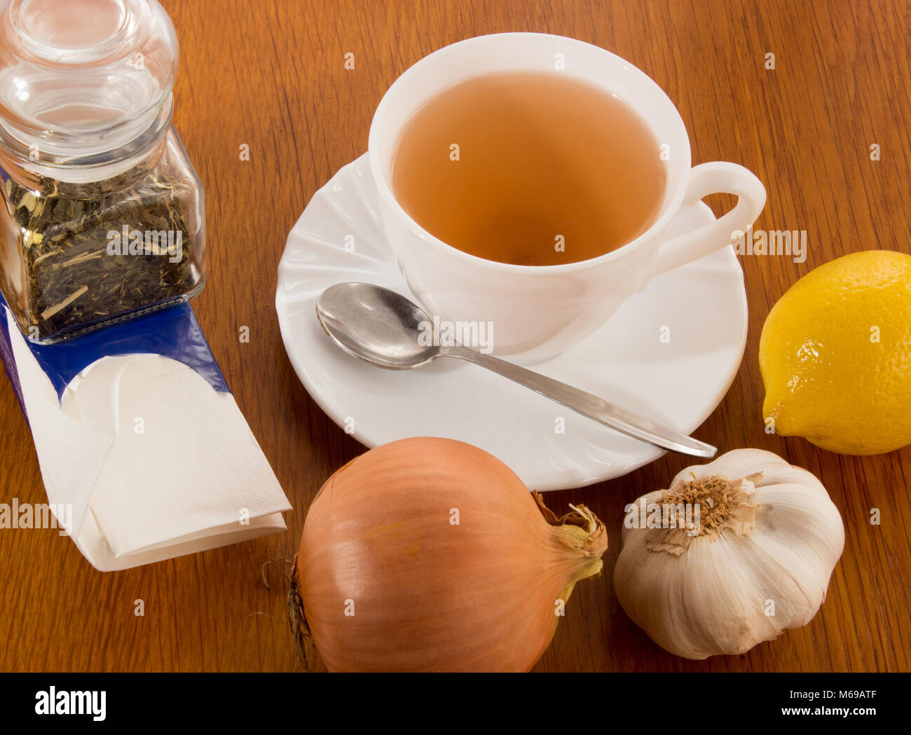 Una taza de té con platillo y cuchara, limón, cebolla, ajo, una dosis de cristal con té, pañuelos de papel. Todo en contra de pescar un resfriado en la madera de Foto de stock