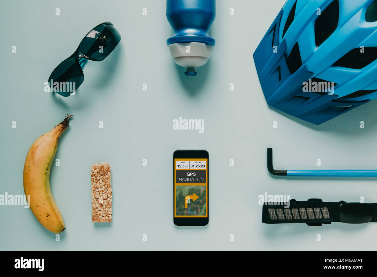 Accesorios ciclismo sobre fondo azul, y ruta GPS en la pantalla del teléfono móvil. Foto de stock
