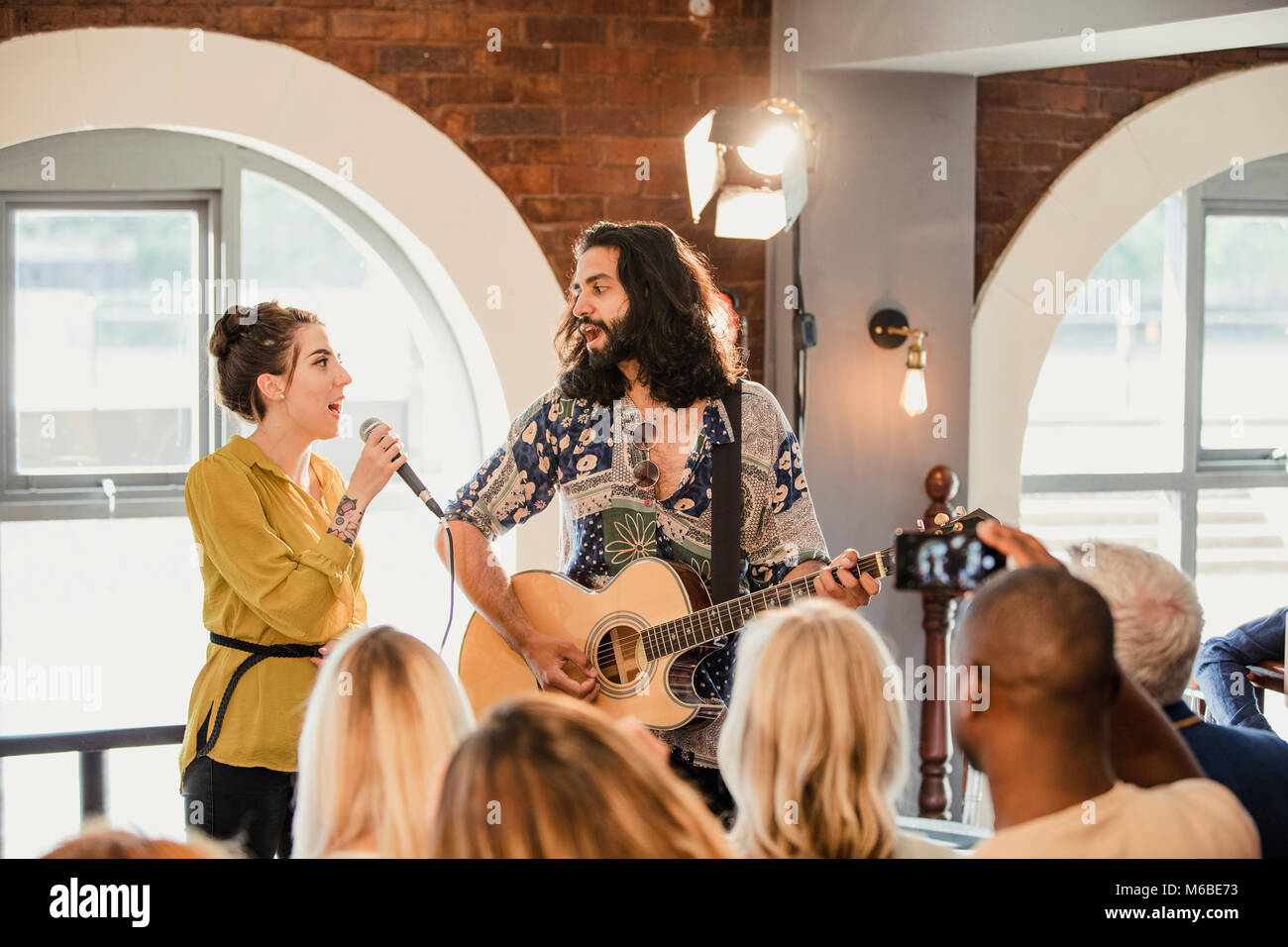 Los invitados a la boda están disfrutando algunos entretenimiento acústicos. Hay un hombre tocando la guitarra y una mujer cantando y todo el mundo está viendo y tomar videos. Foto de stock