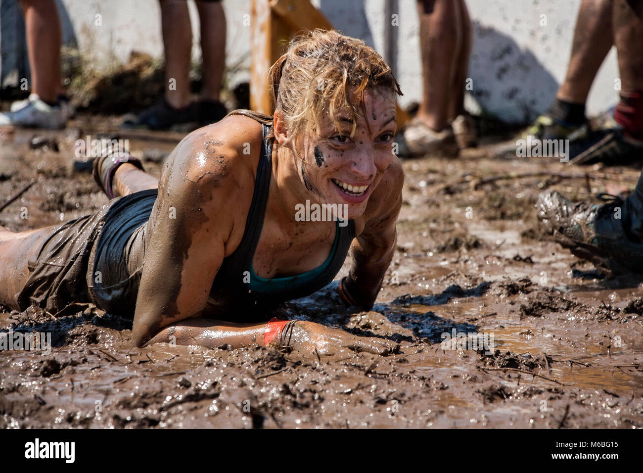 Mujer joven arrastrándose en el lodo; participación en deporte extremo, fuerza física desafío Foto de stock