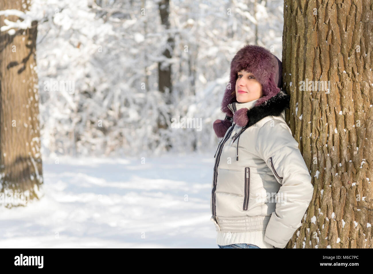 Mujer sonriente está de pie en el bosque llevando un sombrero de piel y una chaqueta blanca. Las nieves del invierno. El sol brilla. Día, Rusia. Foto de stock