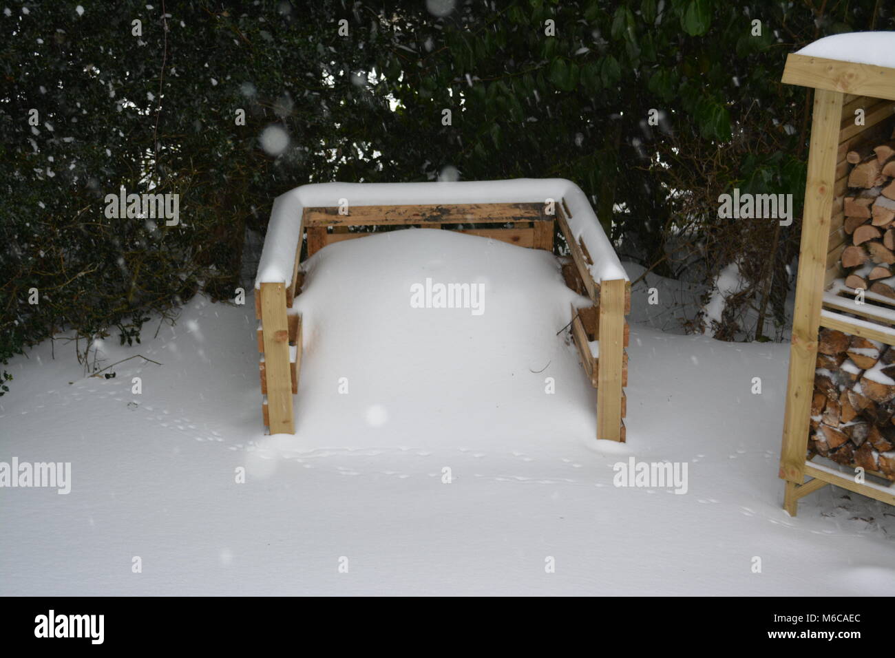 Compostera formado de re-paletas usadas y parte de la tienda con un registro en el jardín hecho de madera tratada y cubierta con fuertes nevadas tras la fuerte tormenta Foto de stock