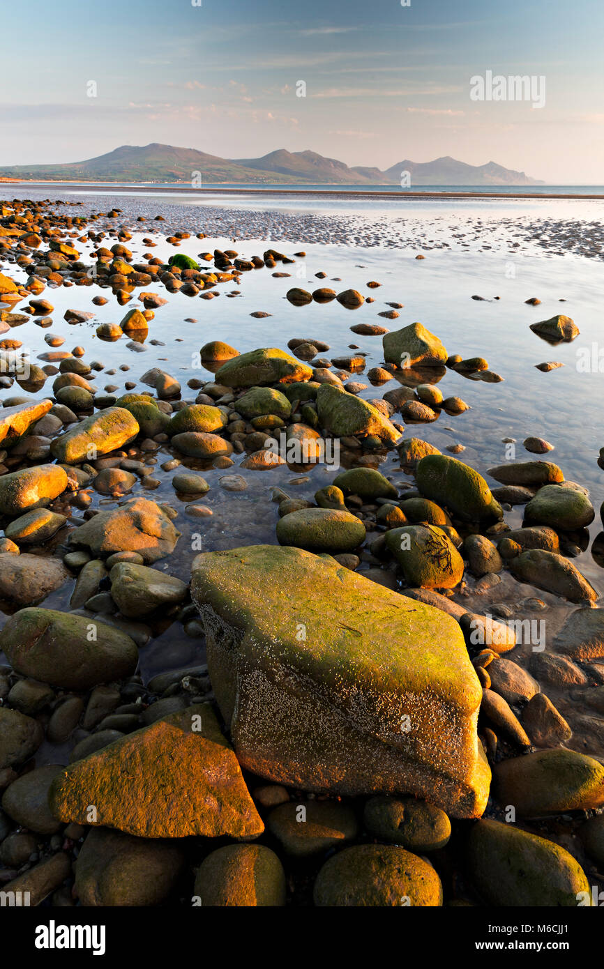 Las rocas de la playa en el Dinas Dinlle en la costa de Gales del Norte, con piscinas, el mar y las montañas Foto de stock