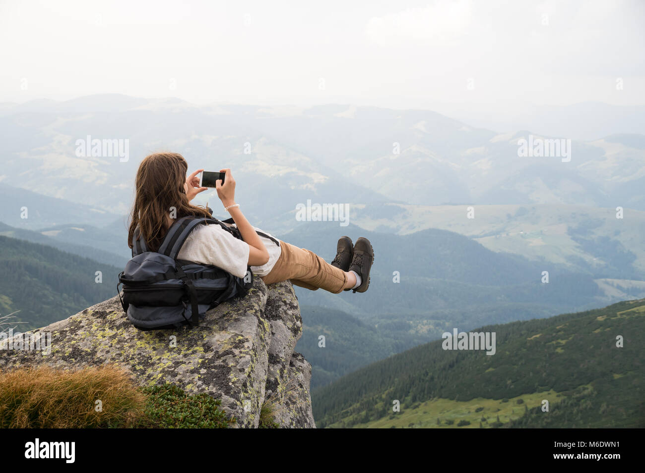 Caminante chica con mochila teniendo autorretrato en hermosos paisajes sobre una roca en los Cárpatos ucranianos Foto de stock