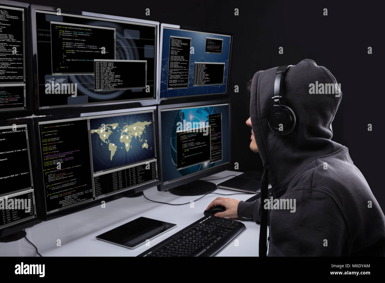 Vista trasera de un hacker utilizando varios equipos para robar datos en Office Foto de stock
