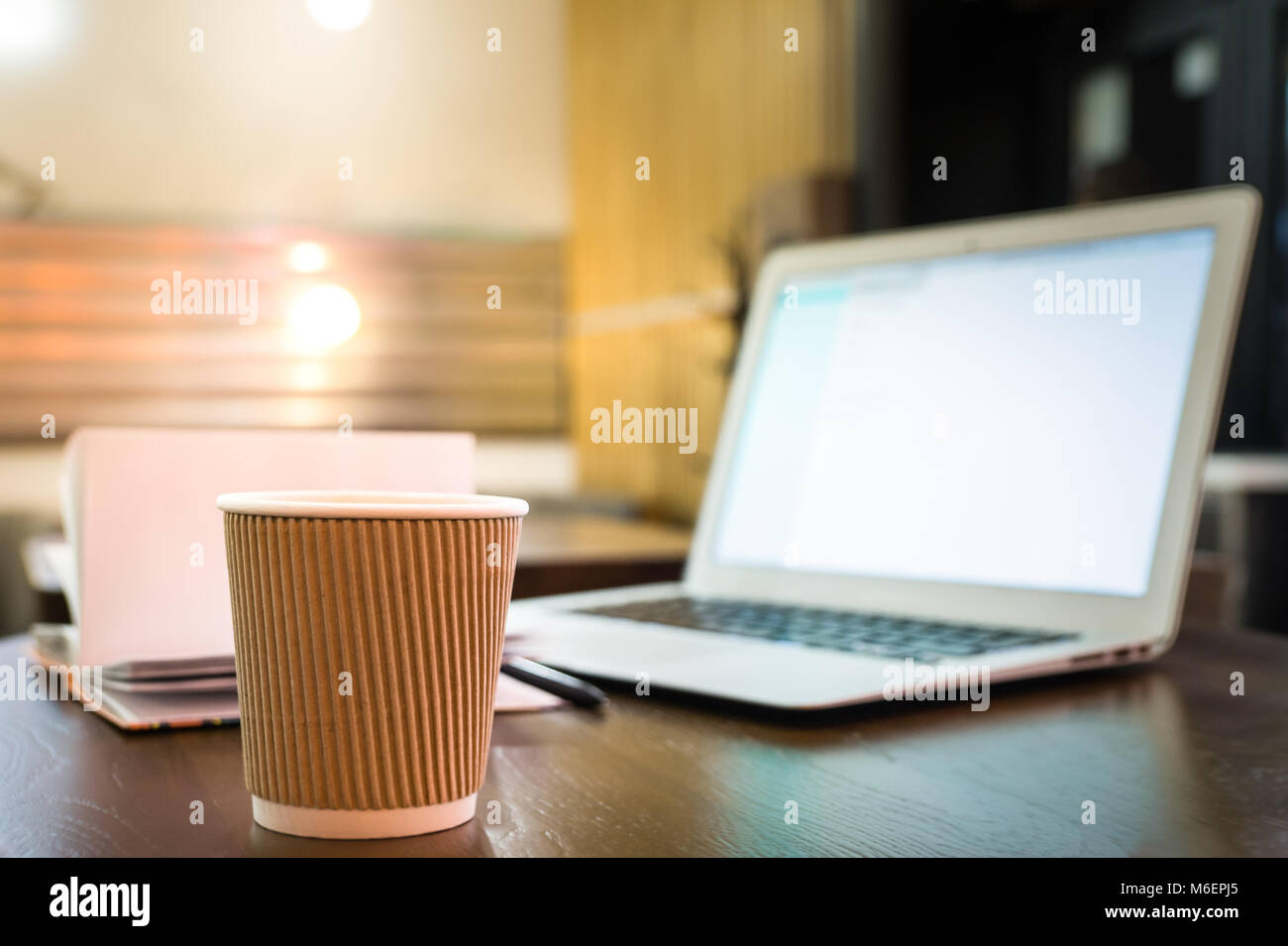 Taza de café y ordenador portátil sobre la mesa de café. Ordenador portátil, Note Pad y vaso de papel en la noche de fondo interior Foto de stock