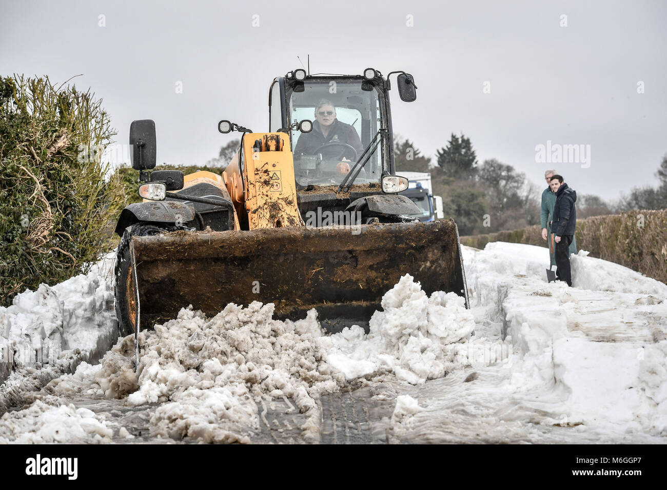 Una JCB se usa para raspar la superficie de la carretera y después de limpiar la nieve los vehículos quedaron atrapados en la nieve en Draycott estrecha, entre Draycot Foliat y Ogbourne St George, cerca de Marlborough, Wiltshire, donde la carretera se utiliza como ruta de desvío debido a la A346 en el nevado restantes. Foto de stock