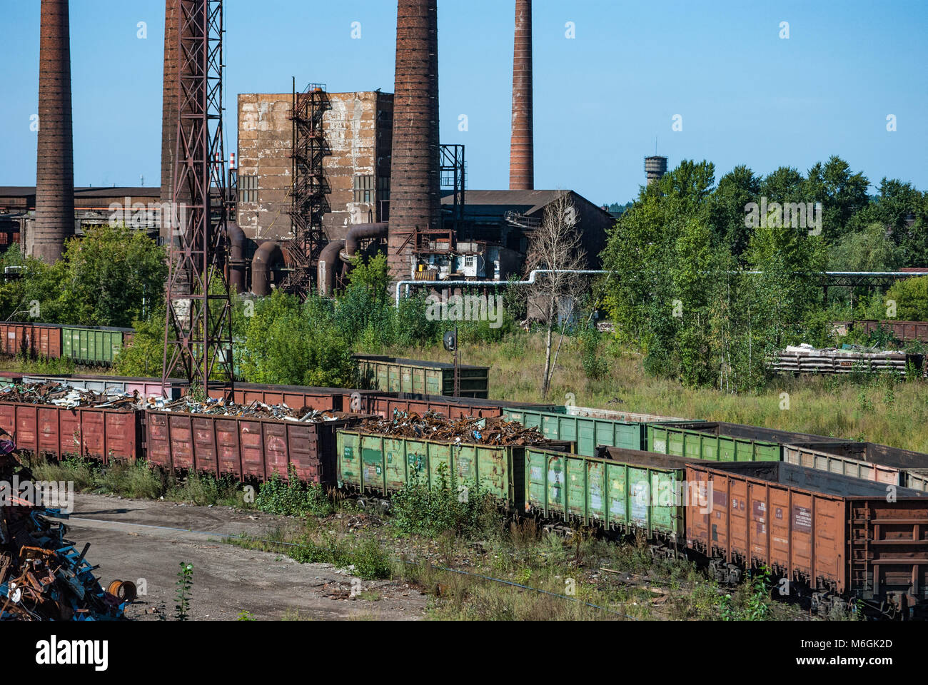 Complejo industrial abandonado, con estacas de humo altas y desgastadas que se elevan sobre los edificios en ruinas contra un cielo azul claro Foto de stock