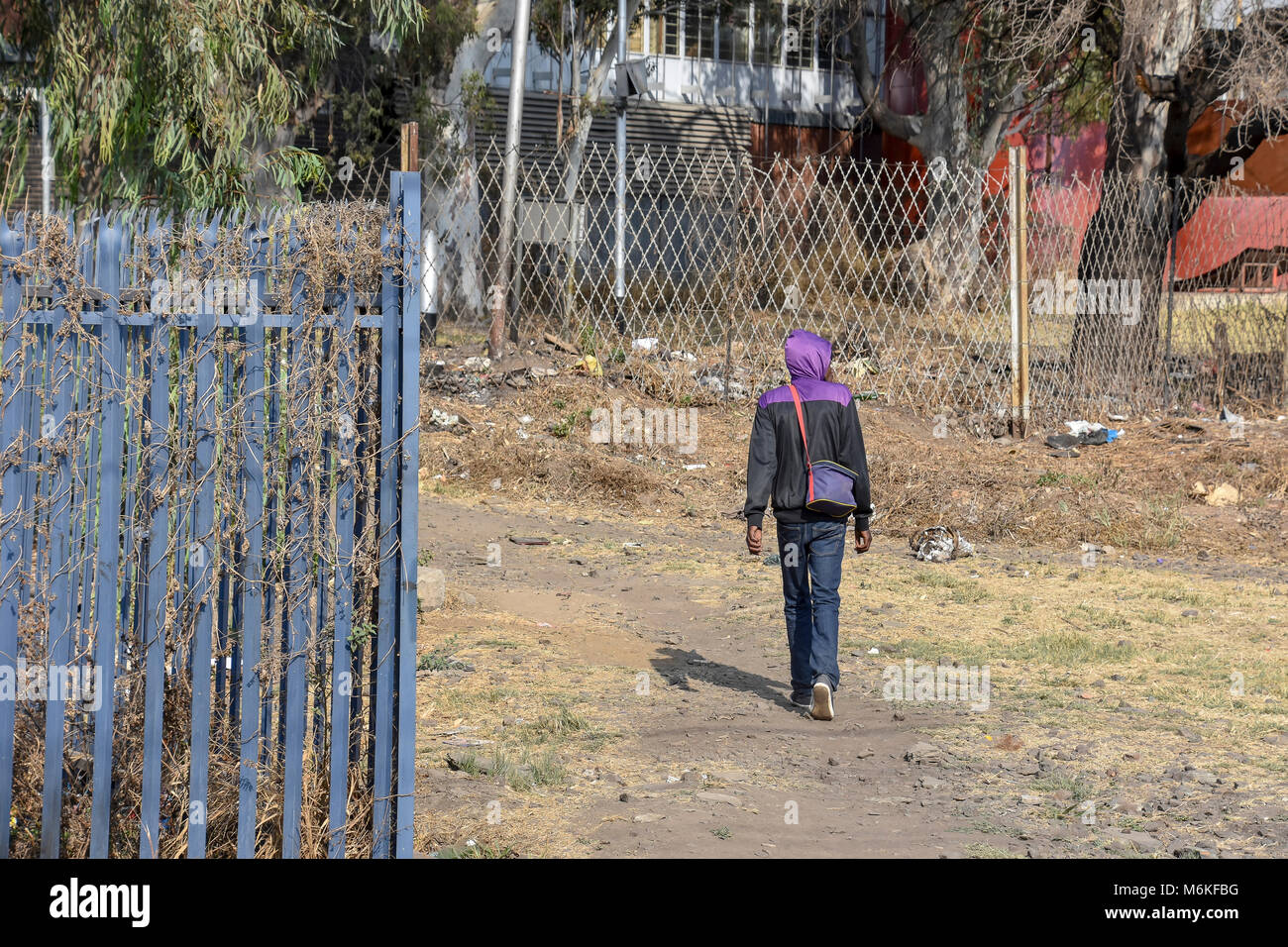 Un hombre caminando cerca de una puerta con una alambrada de púas en Pretoria Sudáfrica utilizadas como cercas de acero construidos con bordes afilados o puntos utilizados para pr Foto de stock