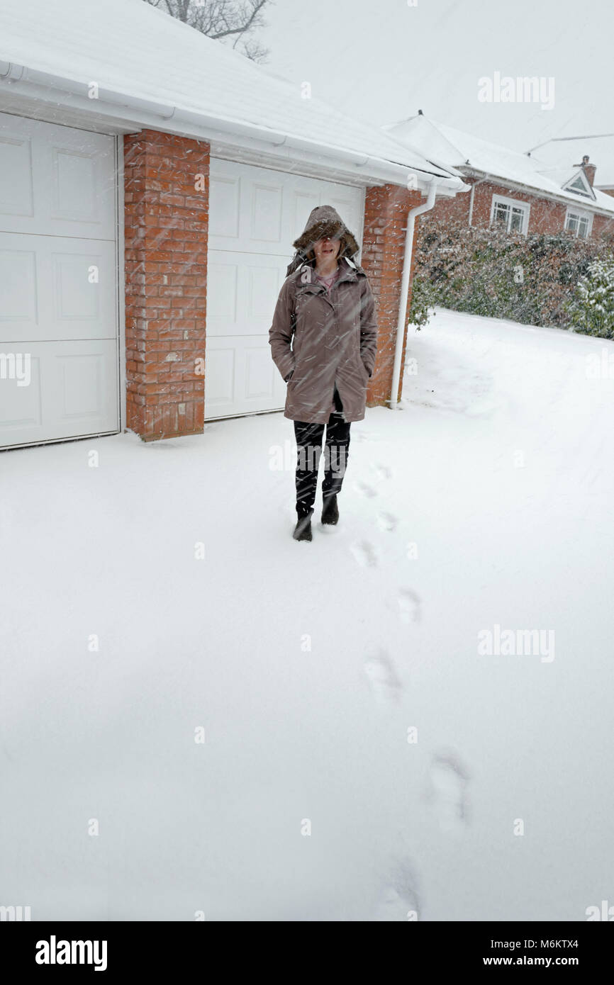 Mujer caminando desde el garaje en nieve UK Foto de stock