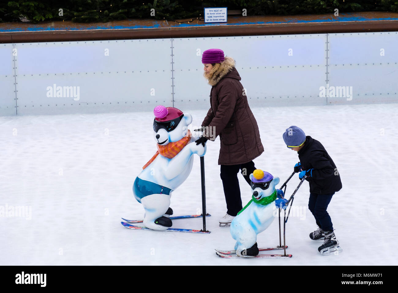 Mujer y niño skate en un anillo de patinaje sobre hielo pública utilizando un marco de apoyo. Karlsplatz, Munich, Baviera, Alemania, Europa Foto de stock