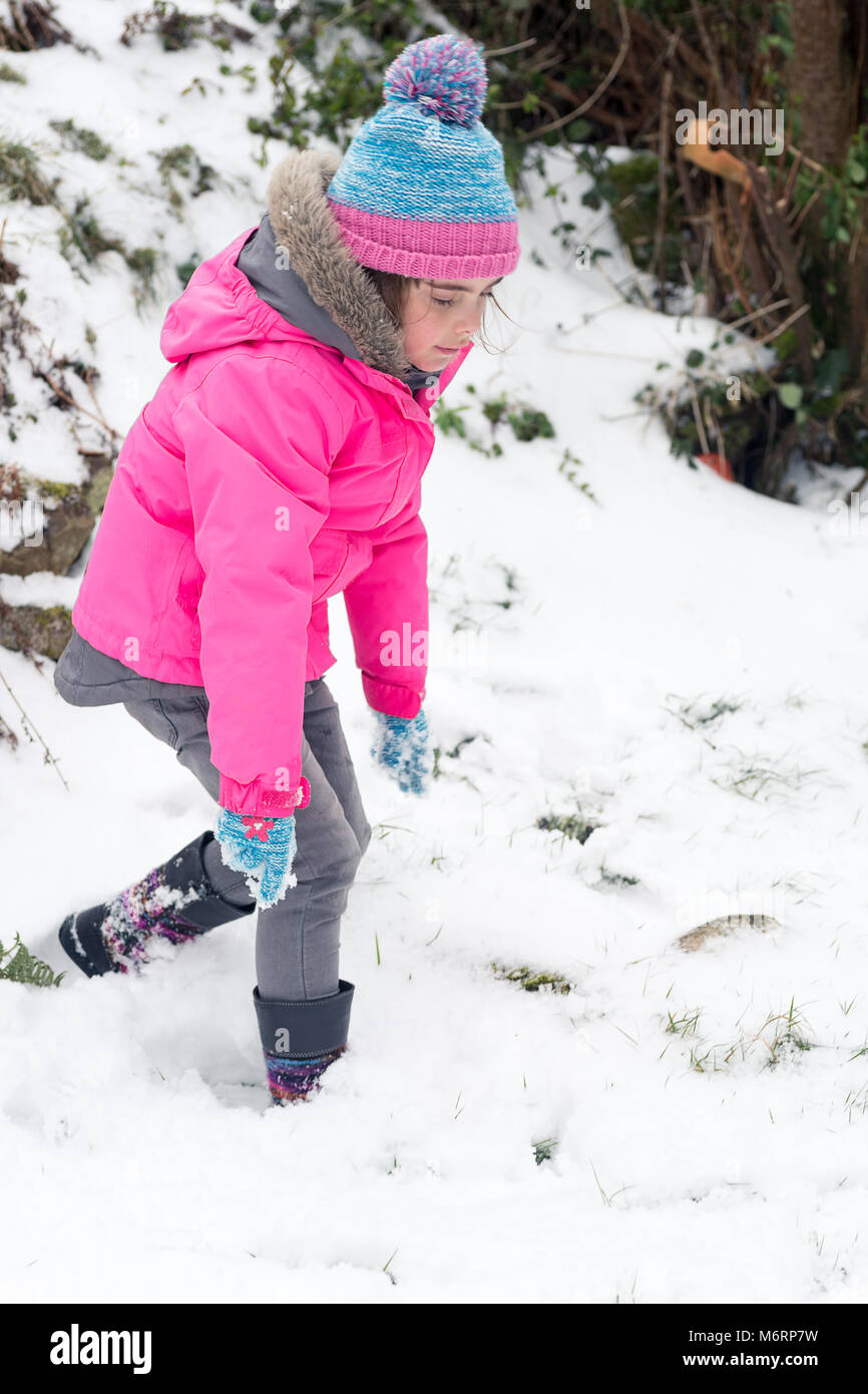 Niña en traje de nieve blanco y sombrero rosa, botas y guantes en el parque  de invierno de nieve.