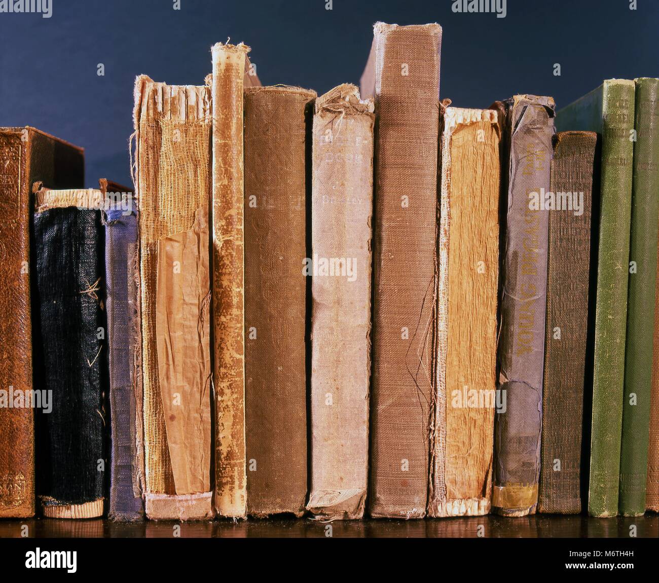 Los viejos libros en una estantería mostrando signos de desgaste y envejecimiento. Foto de stock