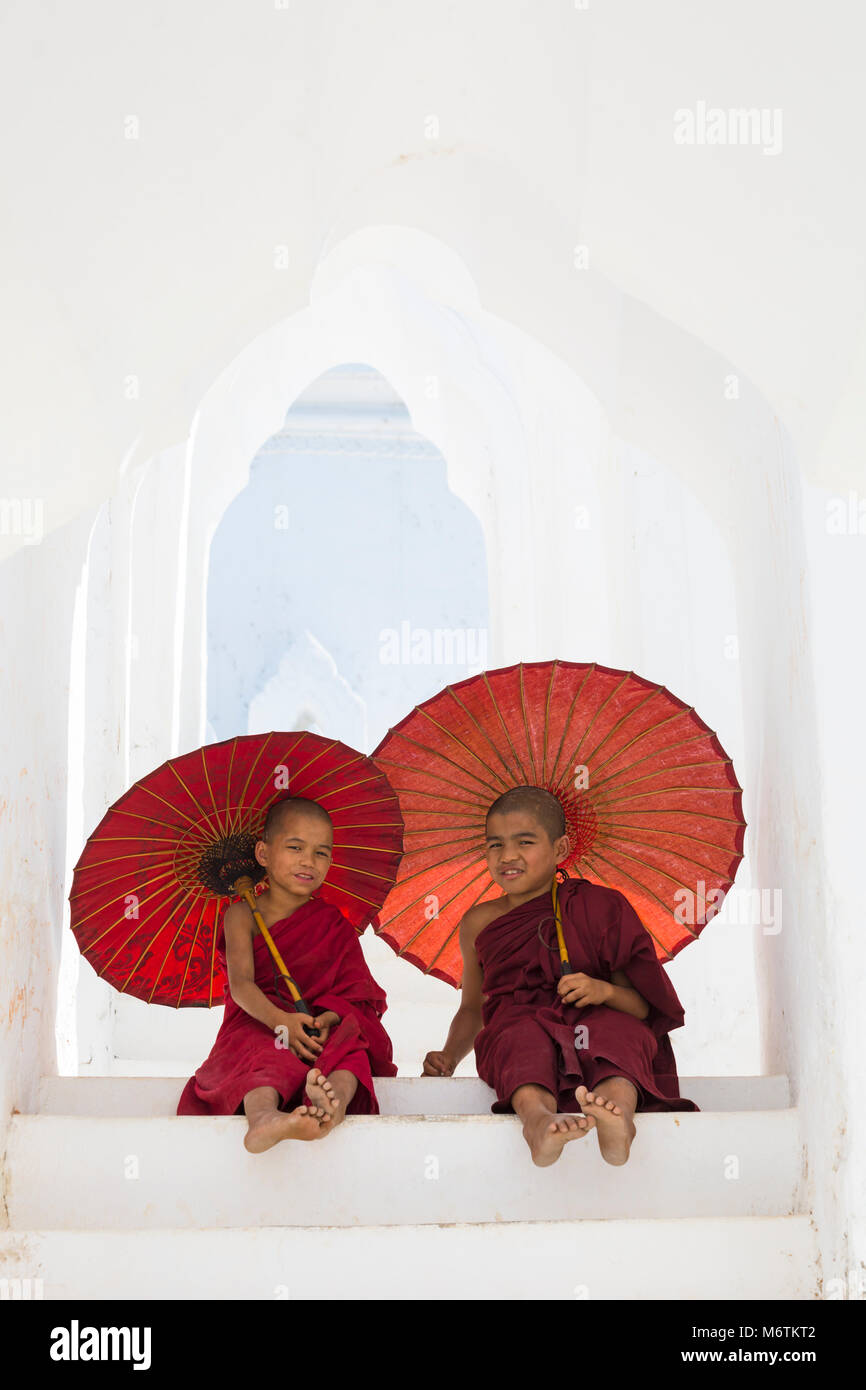 Joven novicio monjes budistas sosteniendo sombrillas en la Pagoda Myatheindan (también conocida como la Pagoda de Hsinbyume), Mingun, Myanmar (Birmania), Asia en febrero Foto de stock