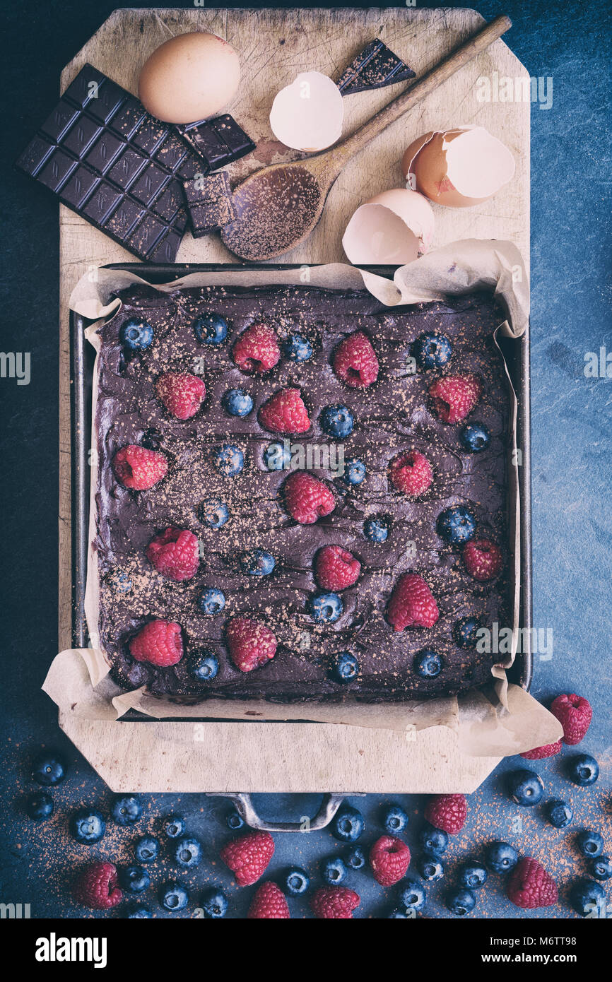 Chocolate crudo casero de frambuesa y arándano brownie mezcla en una bandeja para hornear con los ingredientes sobre un fondo de pizarra Foto de stock