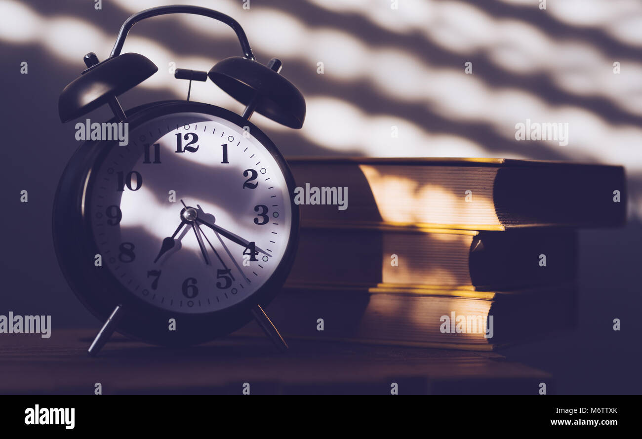 Reloj con alarma y libros antiguos en las estanterías del mañana, el concepto de la educación y la lectura Foto de stock