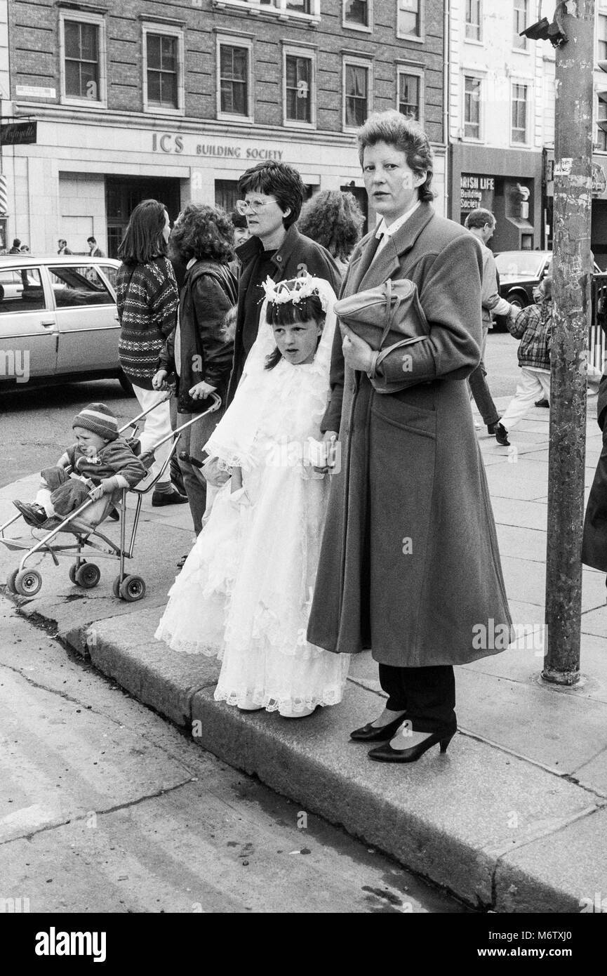 Niña vestidos de primera comunión en la esquina de la calle esperando para cruzar la carretera, Westmoreland Street, Dublin, Irlanda, archivo de fotografía de abril de 1988 Foto de stock