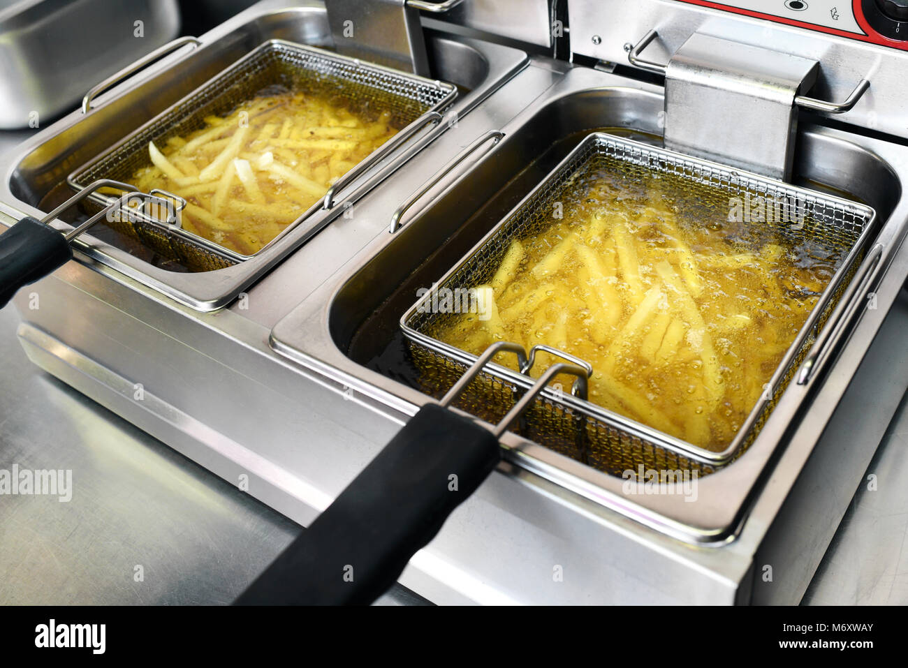 Papas fritas o hojuelas de patatas fritas freír en aceite en una freidora metal comercial en un restaurante como acompañamiento de las comidas Foto de stock