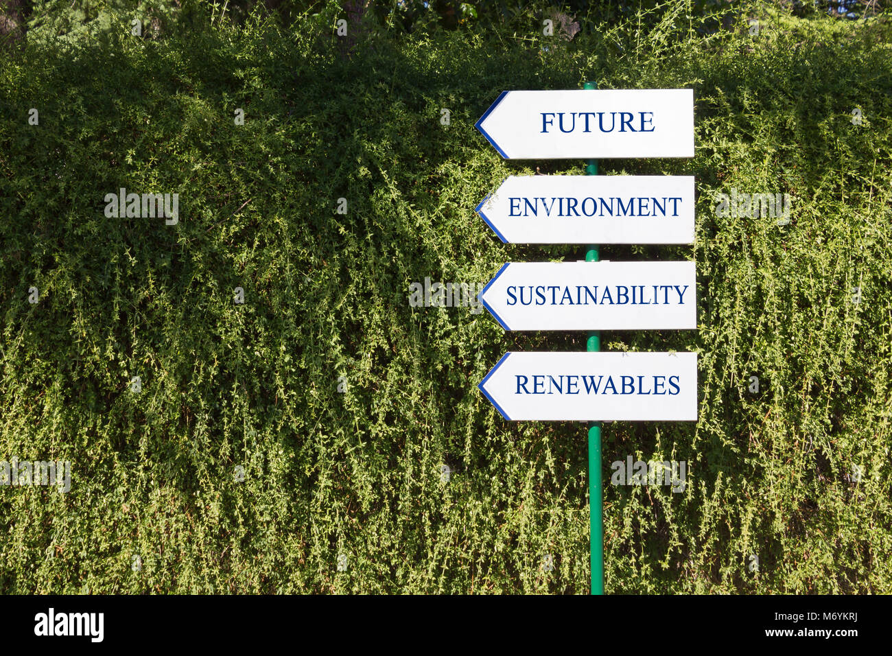 Cuatro señales de dirección blanco contra una pared reductor indicando los objetivos de la política medioambiental Foto de stock