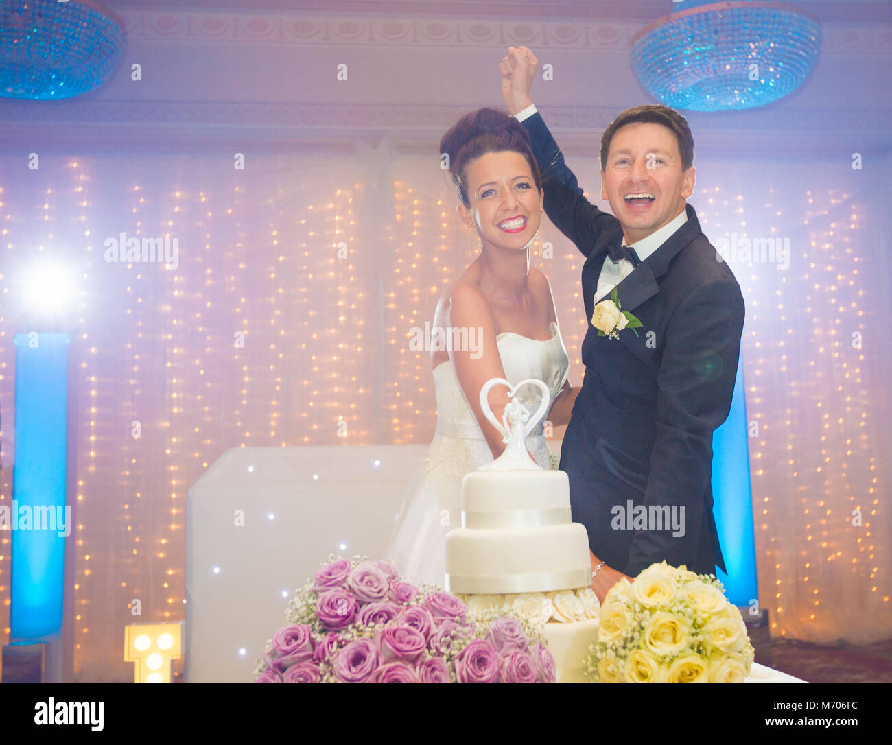 La novia y el novio sonriente cortando el pastel de bodas en el día de su boda Foto de stock